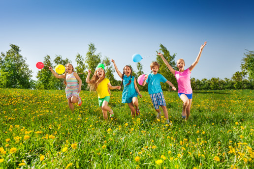Happy excited five children with balloons running in green field with yellow flowers in summer